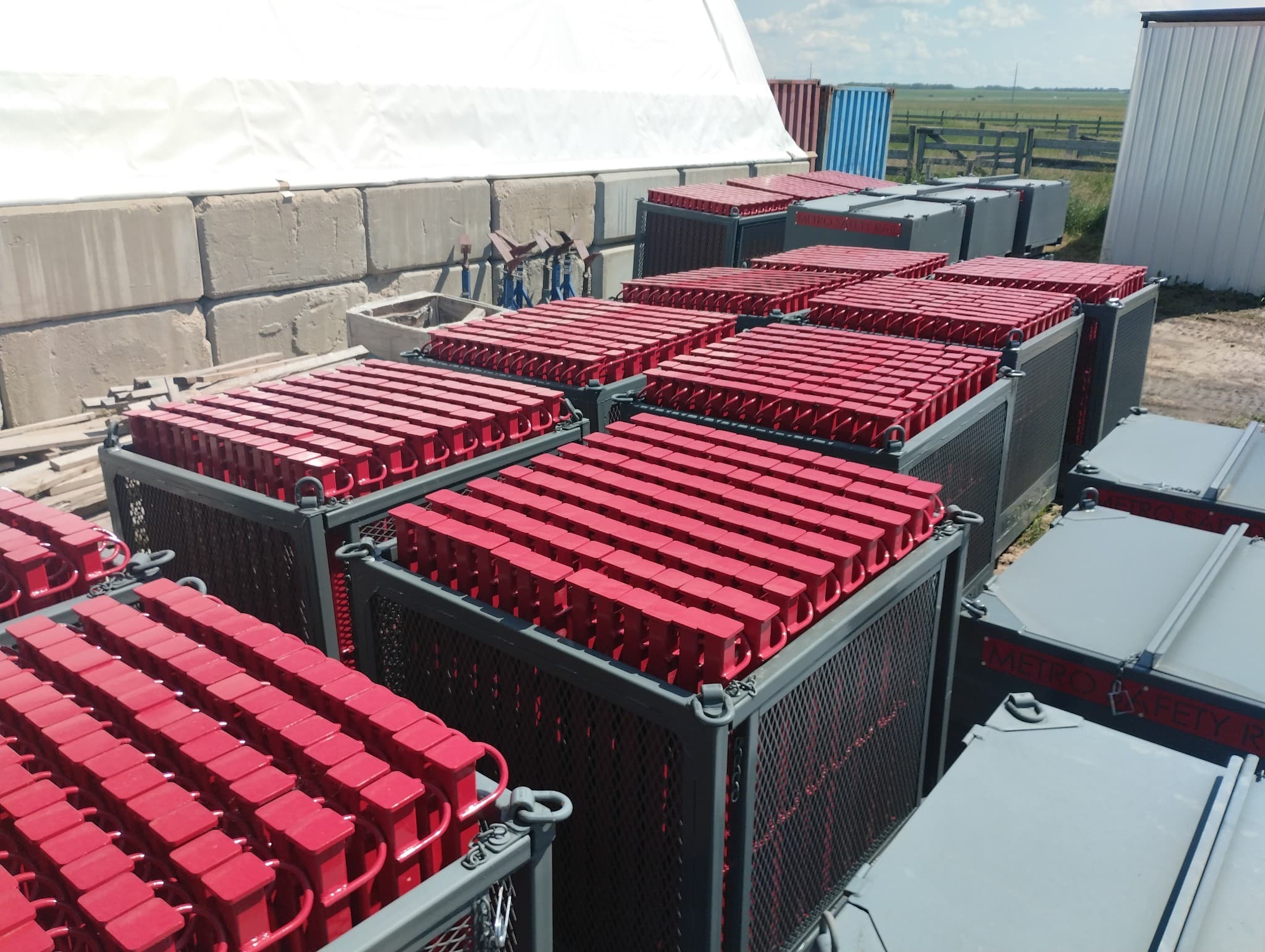 Steel transport containers packed with red guardrail stanchions, staged in rows at a laydown yard.
